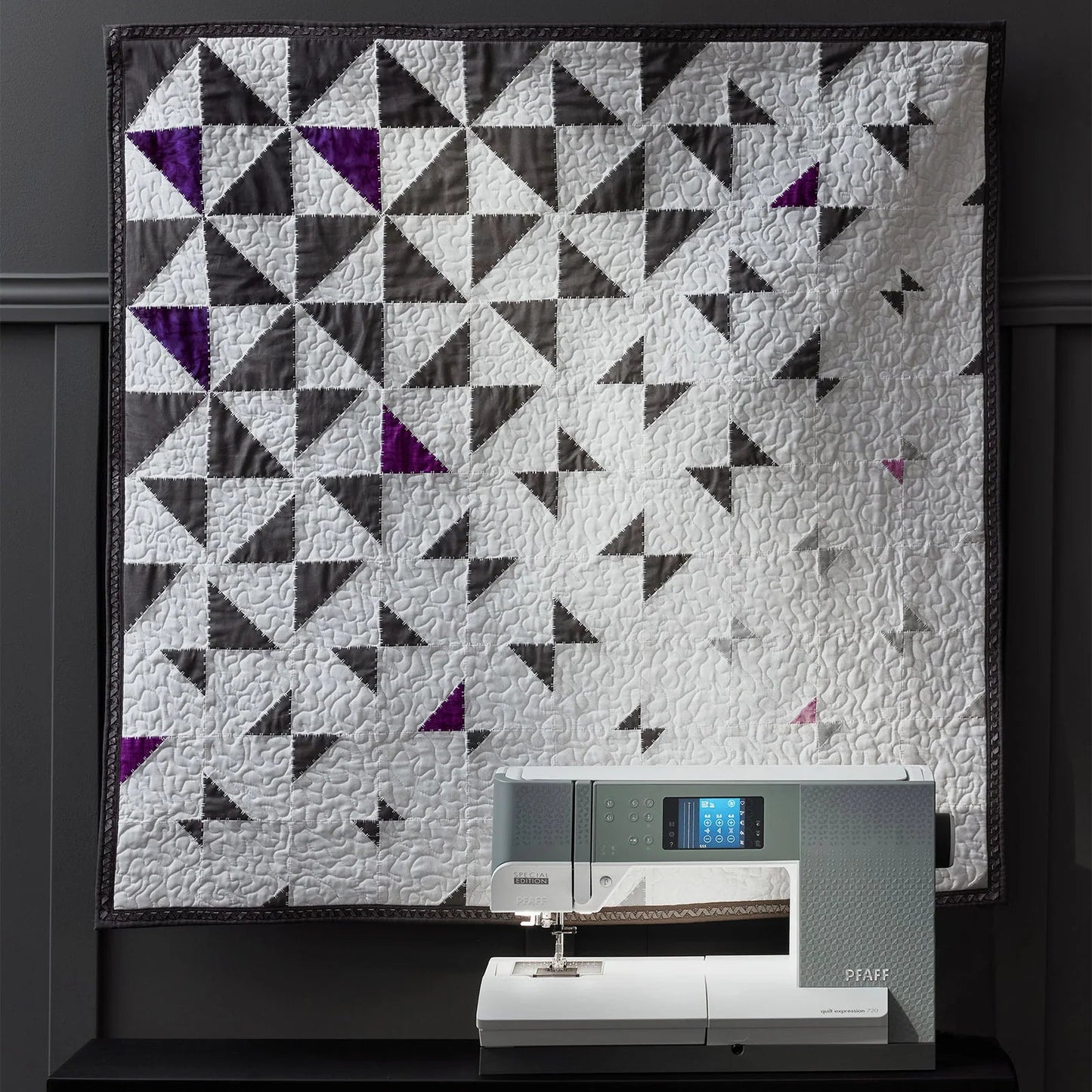 Quilt with geometric pattern displayed above a sewing machine on a dark background