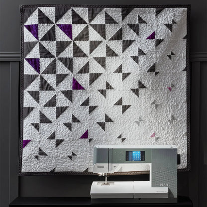 Quilt with geometric pattern displayed above a sewing machine on a dark background