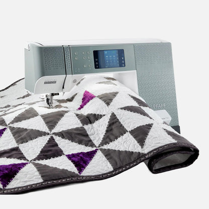 Sewing machine with a quilt featuring geometric patterns on a white background